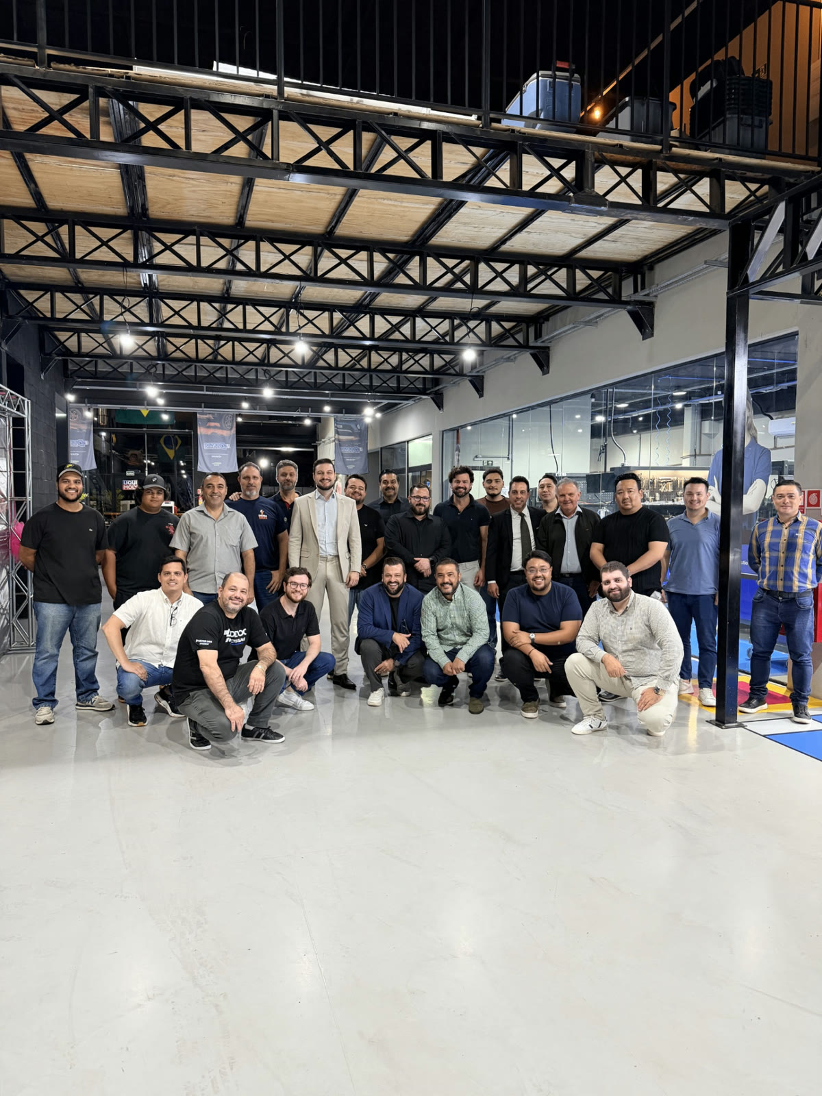 Grupo de empresários posando para foto, parte agachada e parte em pé, dentro de uma oficina moderna