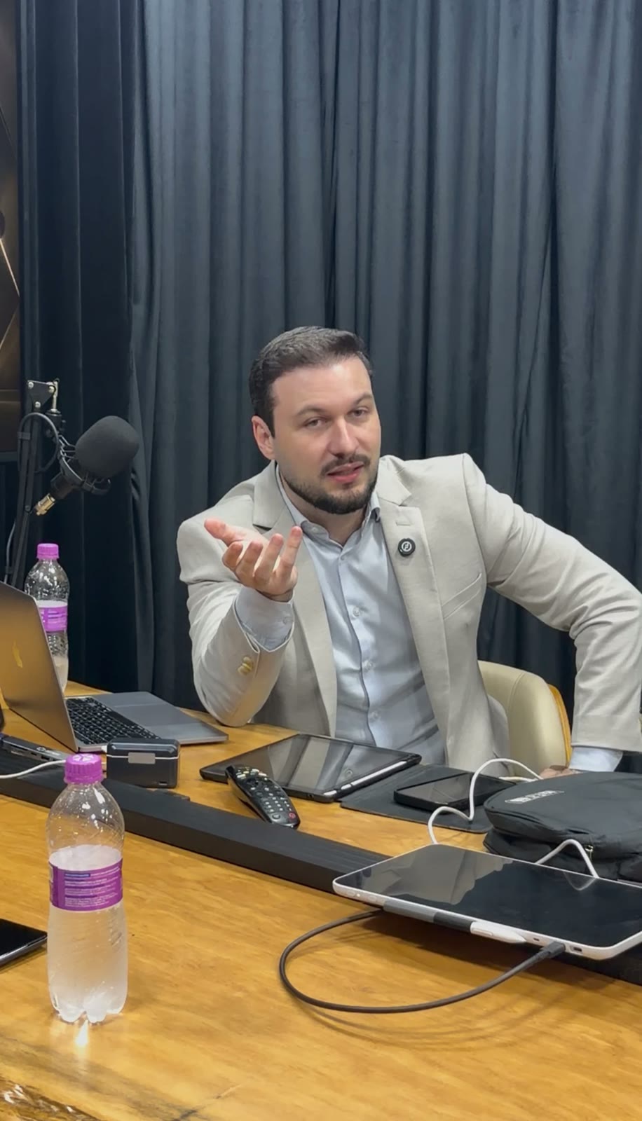 Empresário de terno claro gesticulando enquanto fala em um microfone de mesa
