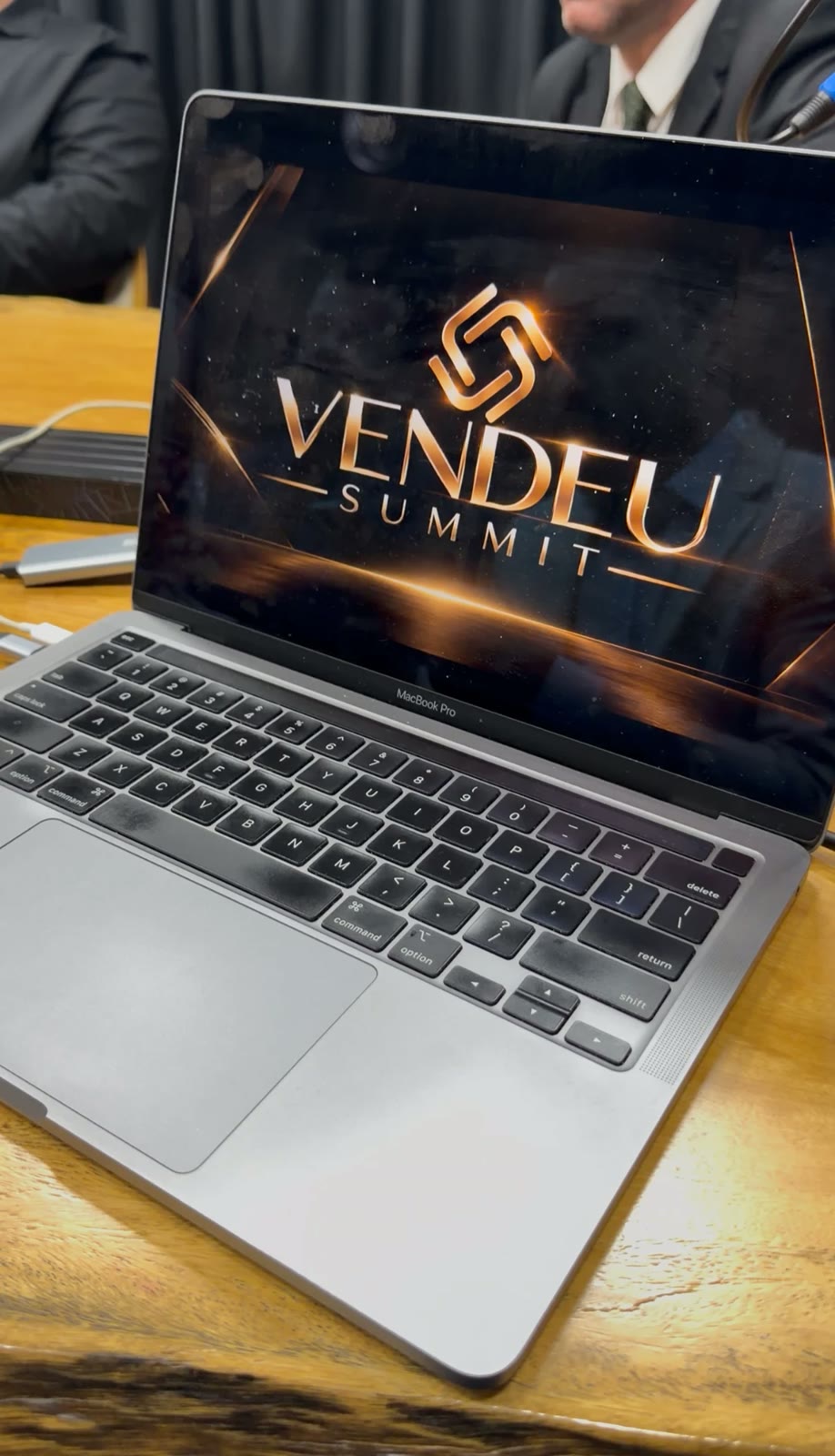 Notebook aberto sobre mesa de madeira exibindo a marca dourada do Vendeu Summit